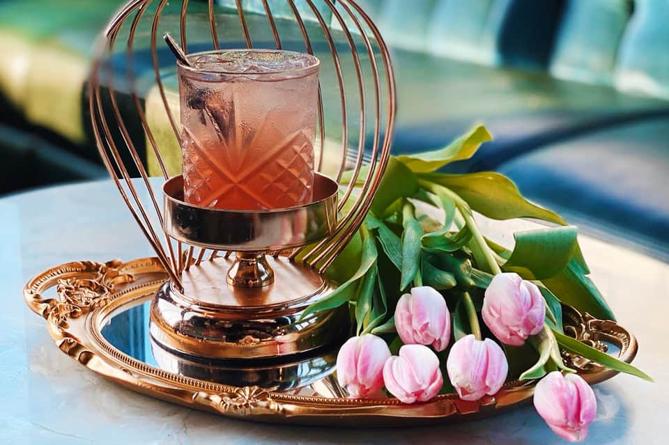 Elegant cocktail in decorative copper holder with pink flowers and ocean view backdrop