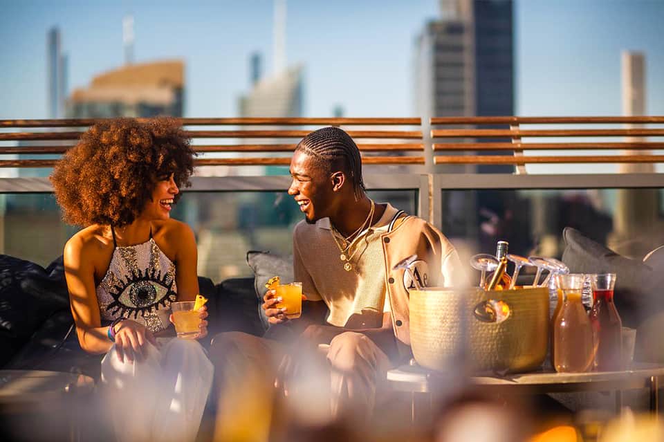 Two people enjoying drinks on rooftop terrace with city skyline in background
