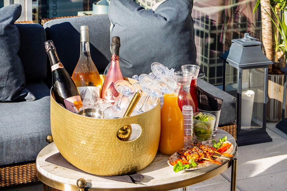 Luxury outdoor lounge with champagne bucket, beverages, and city skyline view