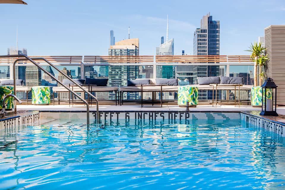 Olympic-sized rooftop swimming pool with city skyline and lounge seating in background