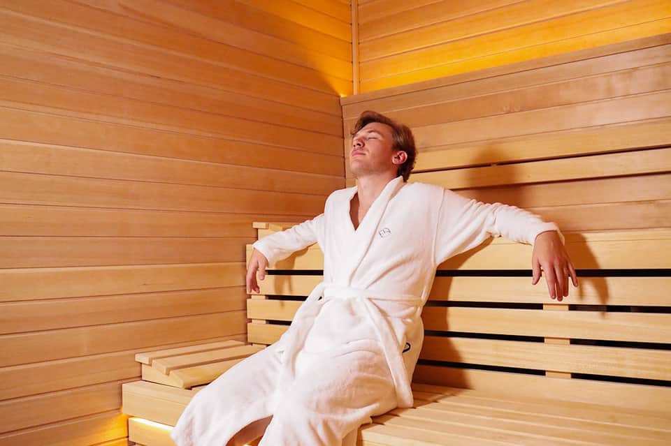 Man relaxing in wooden sauna interior with bench seating and warm lighting