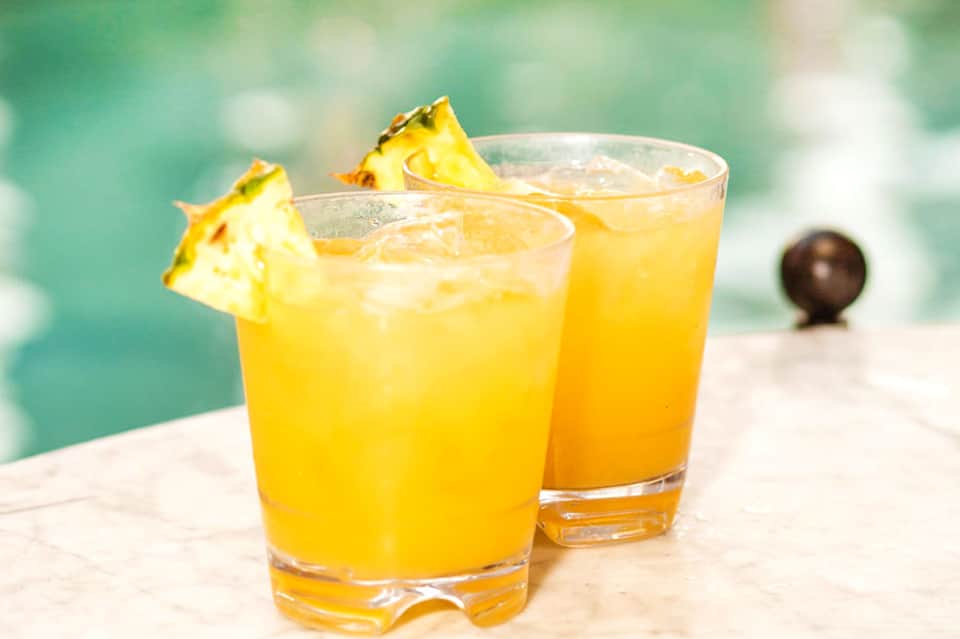 Two tropical pineapple cocktails with ice garnished with fresh pineapple wedges