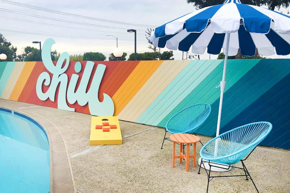 Colorful poolside area with 'Chill' mural, striped umbrella, and turquoise seating