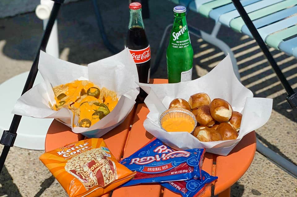 Poolside snacks including tacos, beverages, popcorn, and pretzel bread on chair