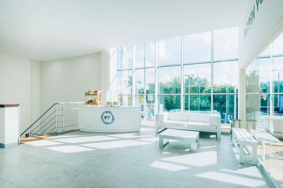 Bright fitness center with large windows overlooking tropical landscaping and reception desk