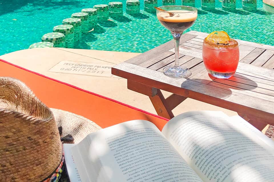 Tropical cocktails on wooden deck overlooking turquoise infinity pool
