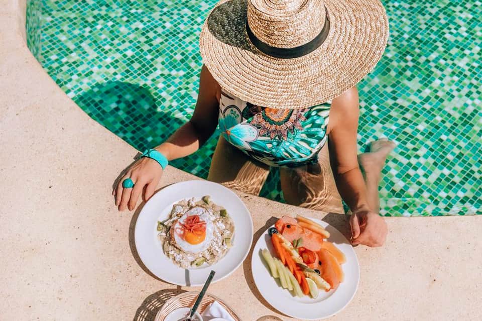 Woman in straw hat poolside enjoying plates of fresh seafood and vegetables