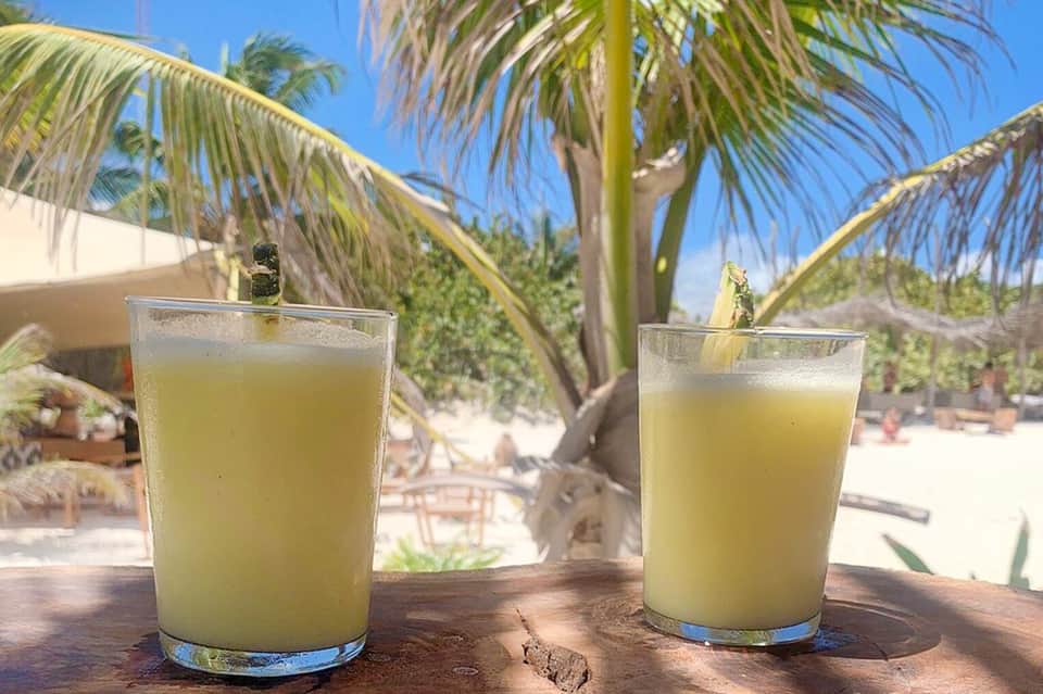 Two glasses of tropical juice on wooden table with palm trees and beach background