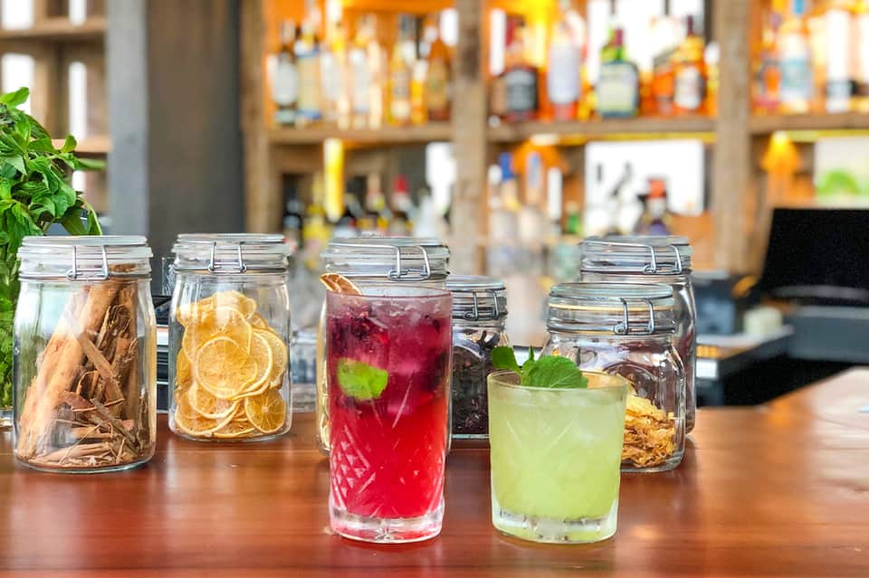 Infused water and herbal tea beverages in glass jars on wooden counter with blurred bar background