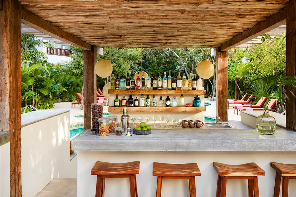 Outdoor tiki bar with wooden beams, liquor shelves, concrete counter, and tropical plants