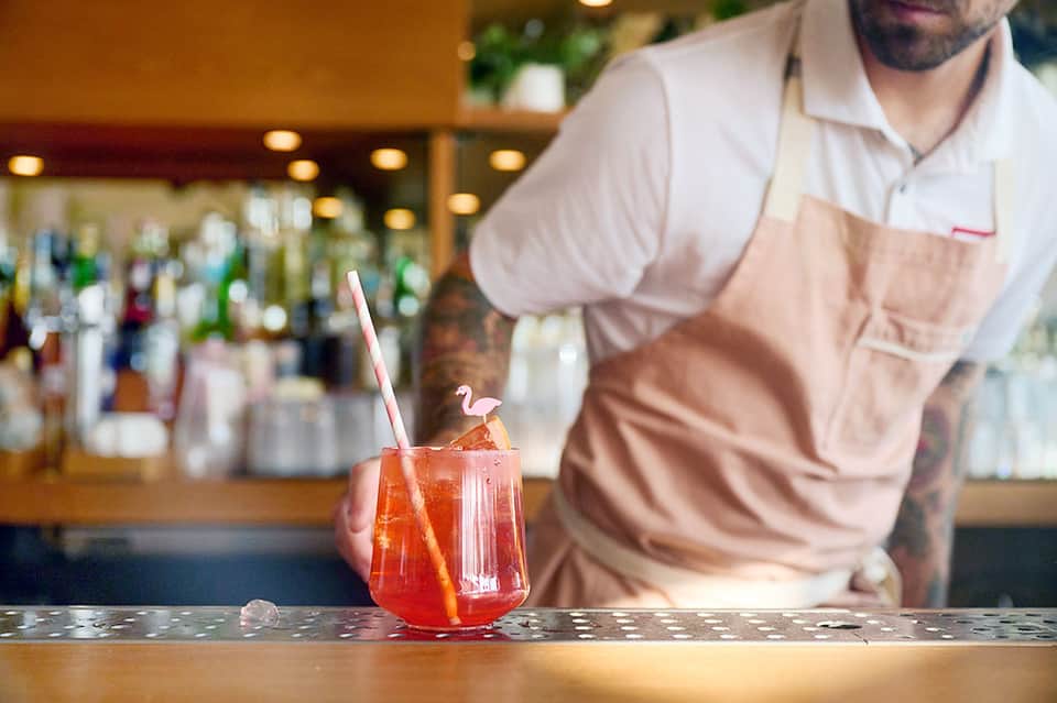 Bartender preparing red cocktail at hotel bar with bottles displayed