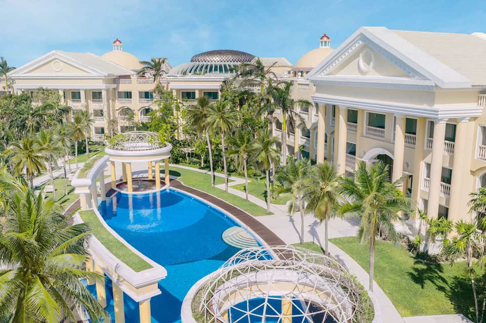 Luxurious resort courtyard with pale yellow neoclassical buildings and blue pools