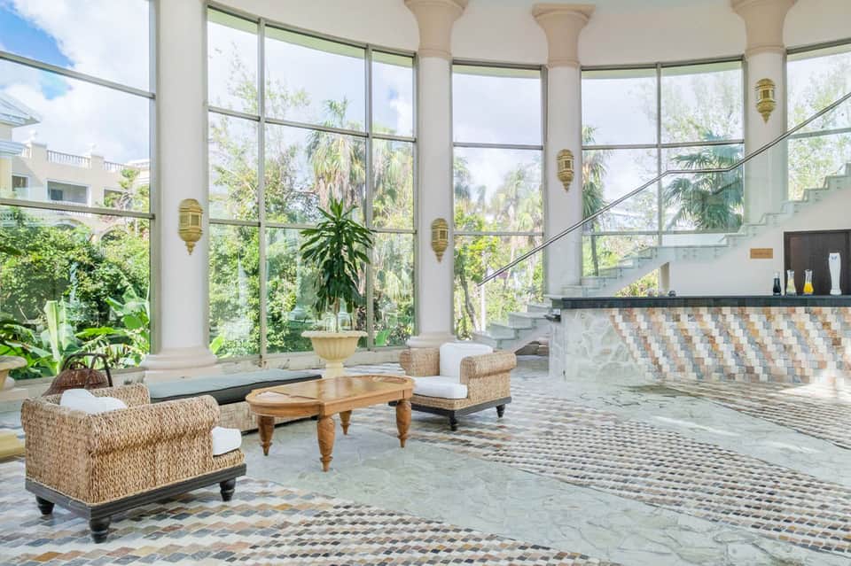Luxury spa interior with floor-to-ceiling windows, marble floors, woven chairs, and hanging lamps