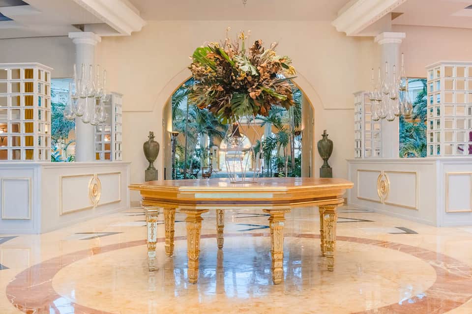 Elegant grand ballroom with golden piano, marble floors, and tropical archway decoration