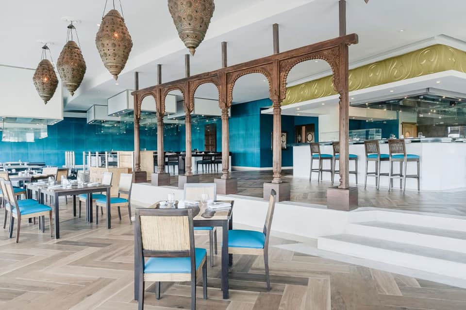 Modern restaurant with carved wooden archway, turquoise backsplash, bar seating, and decorative lanterns