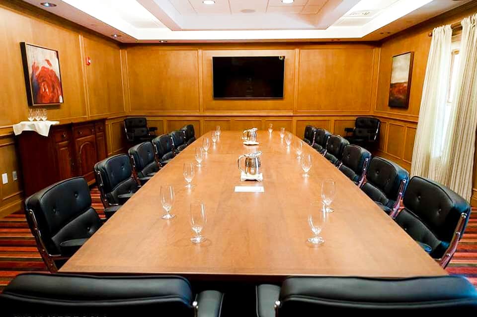 Formal wooden boardroom with long table, black chairs, and flat screen display