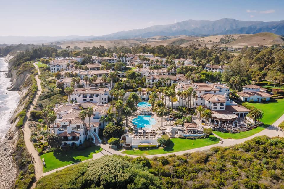 Aerial view of luxury coastal resort with pools, palm trees, and ocean cliffs