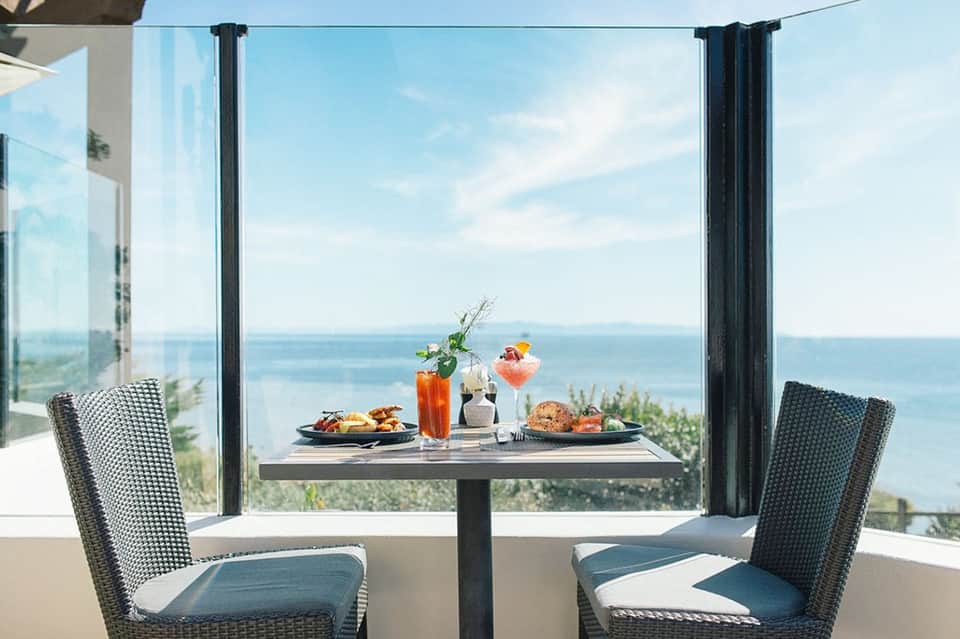 Oceanview dining table with cocktails and food, framed by floor-to-ceiling windows and curtains