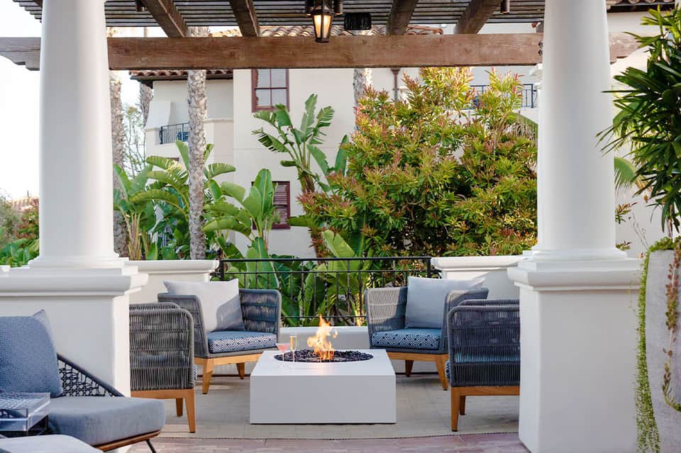 Modern pergola lounge area with gray wicker chairs, fire pit, and tropical landscaping