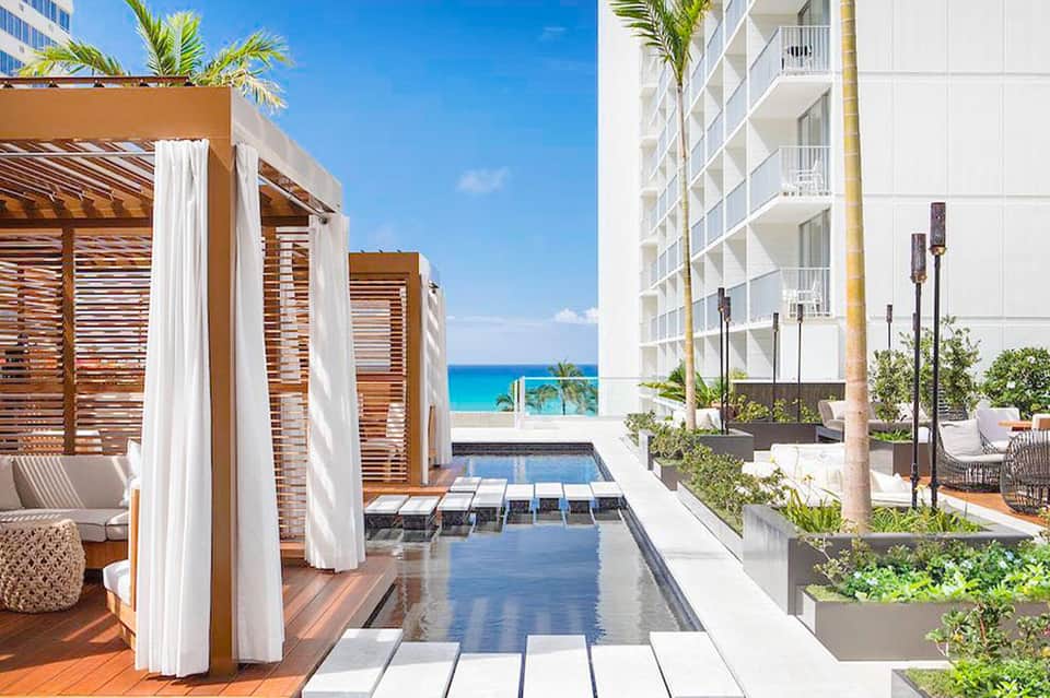 Luxury beachfront resort with infinity pool, wooden pergolas with white curtains, and ocean view
