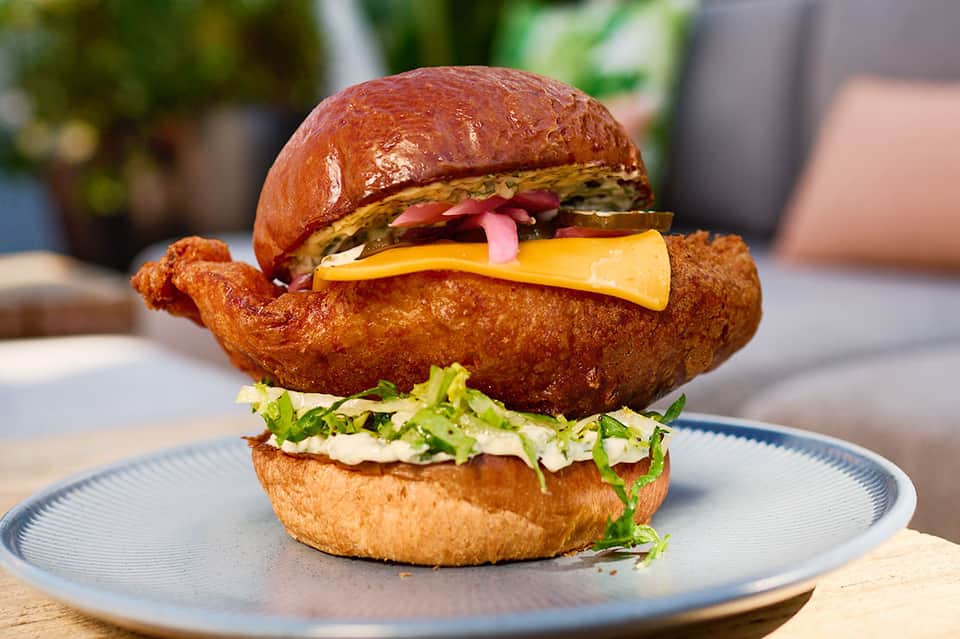 Gourmet fried chicken sandwich with pickled vegetables and cheese on a white plate
