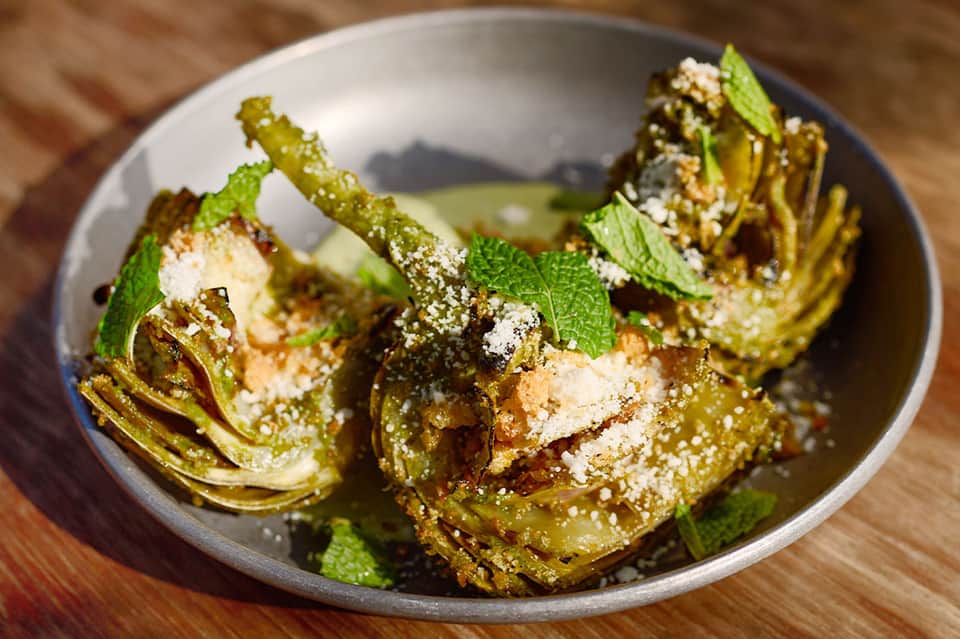 Roasted artichokes with herbs and sesame seeds in white ceramic bowl