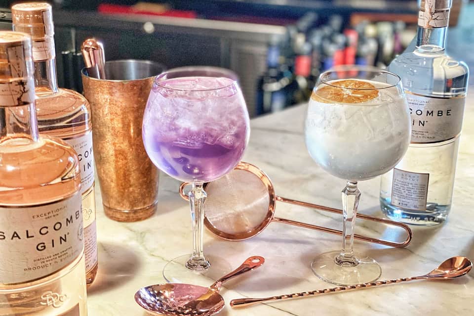 Elegant cocktails including pink gin drink with copper bar tools and premium spirit bottles