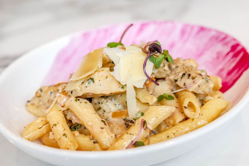 Creamy pasta dish with shaved parmesan and purple microgreens garnish in white bowl on pink napkin
