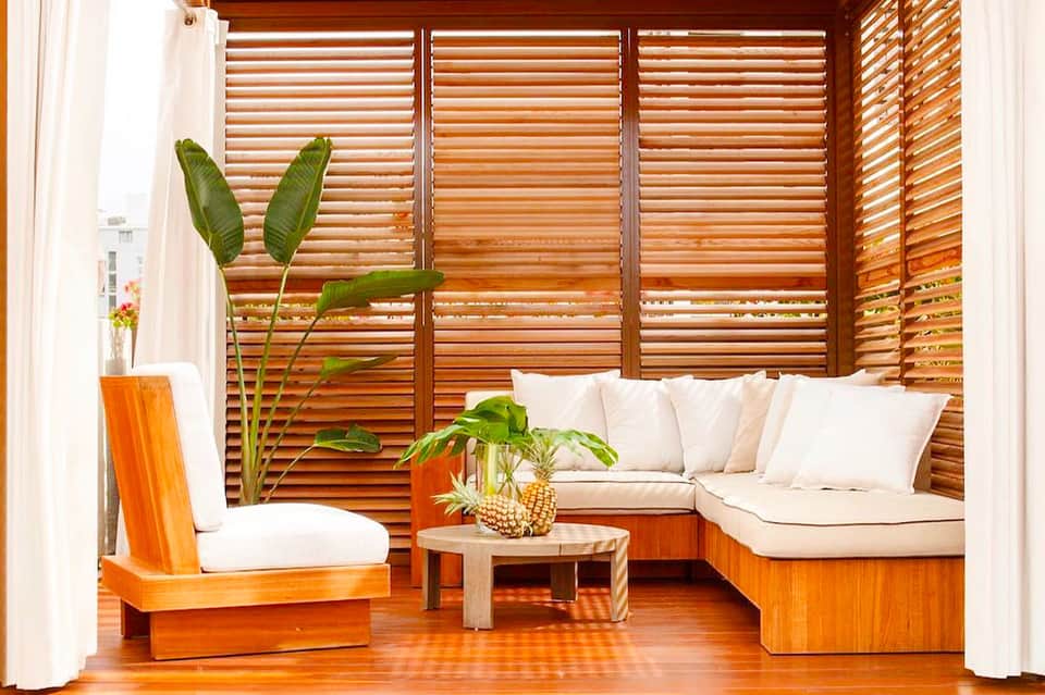 Wooden lounge area with cream cushions, tropical plants, and slatted privacy screens
