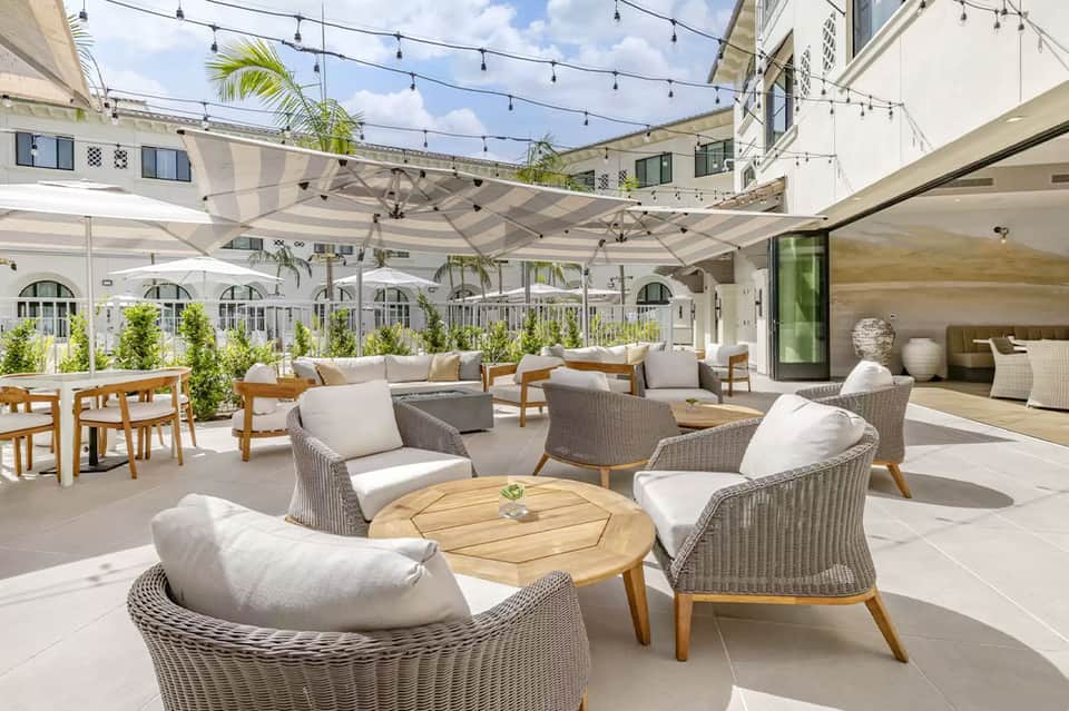 Modern rooftop terrace with woven lounge chairs, wooden tables, string lights, and white umbrellas