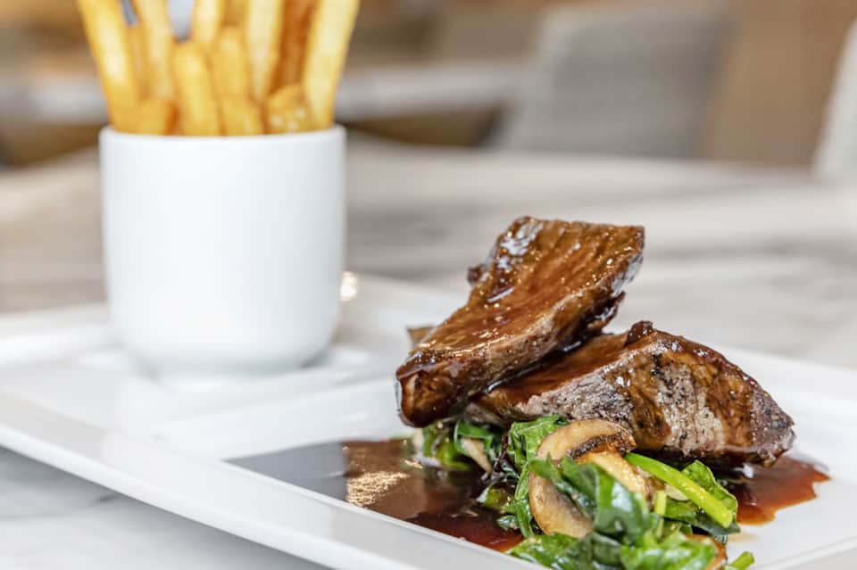 Grilled steak with vegetables and fries served on white plate with refined plating