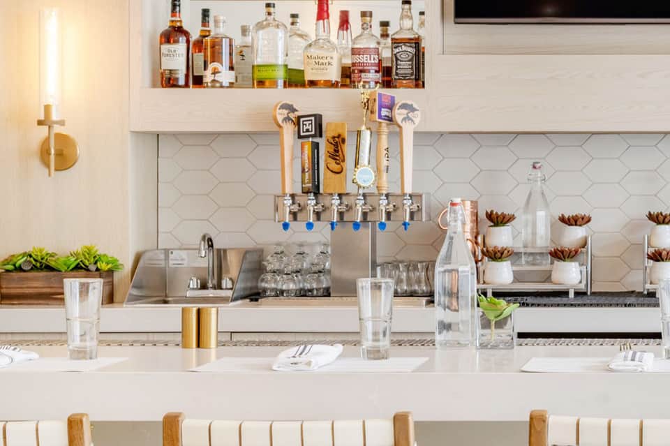 Upscale modern bar with white subway tile backsplash, multiple tap handles, and well-stocked liquor shelves