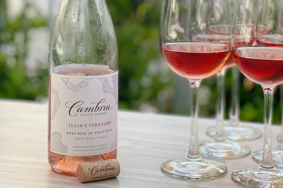 Bottle and glasses of rosé wine on outdoor table with green background