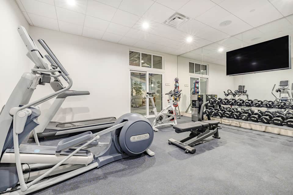 Modern fitness center with cardio equipment, weights, and TV monitor