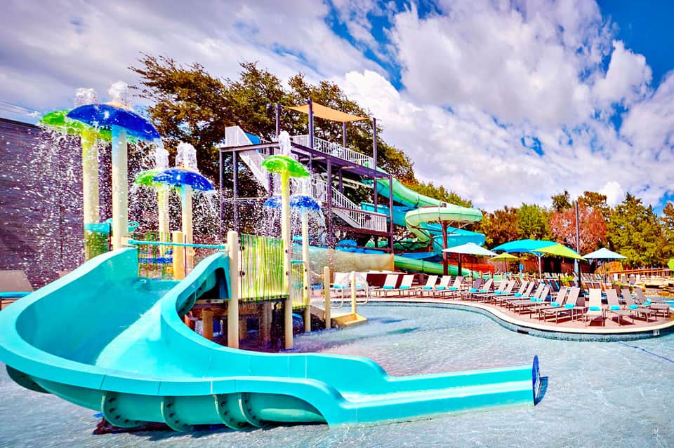 Colorful water slides and splash pad with lounge chairs at outdoor resort pool area
