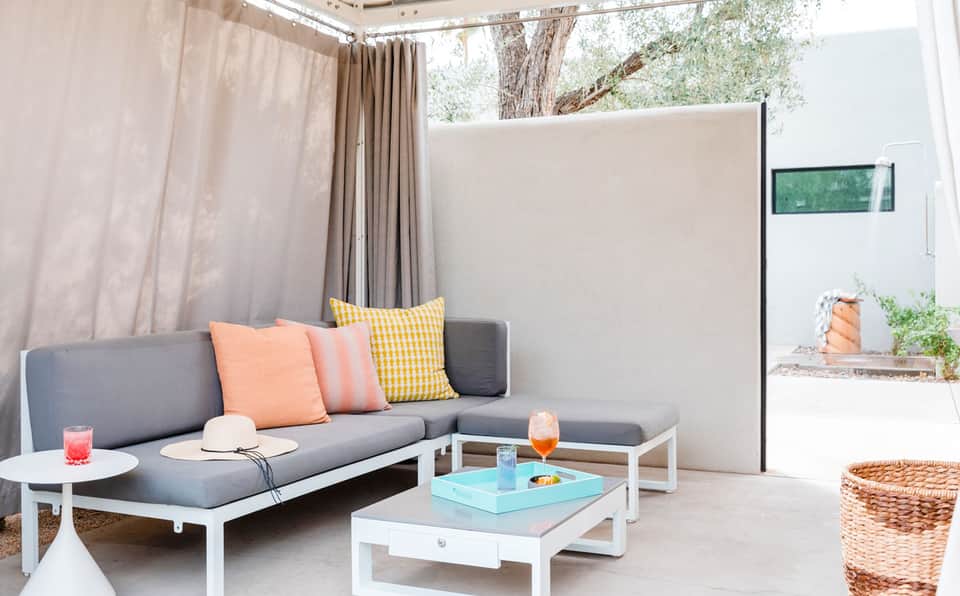 Modern patio lounge with gray sofa, colorful pillows, white tables, and curtained shade