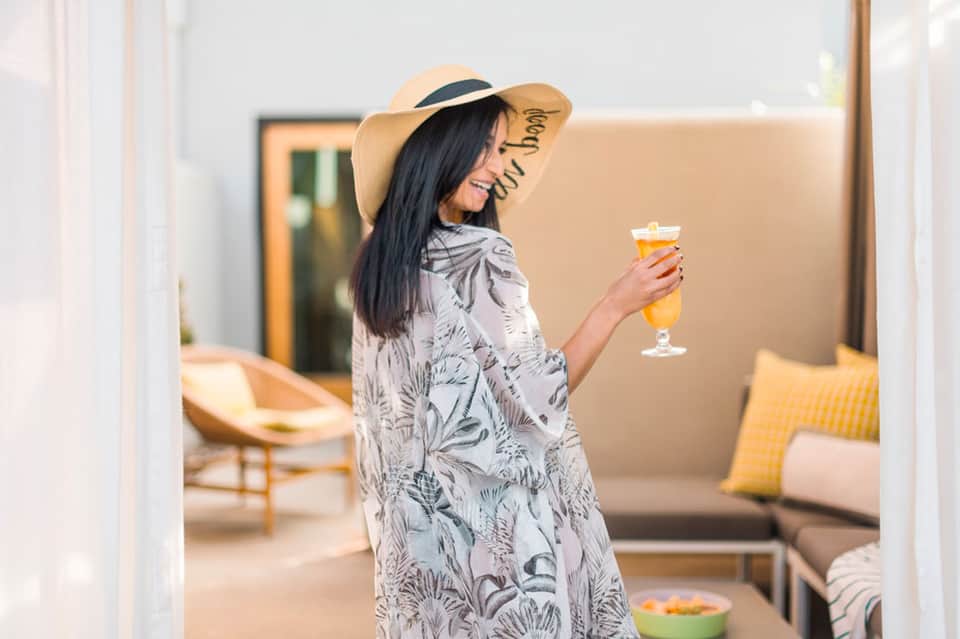 Woman in straw hat holding beverage on sunny resort terrace with lounge seating