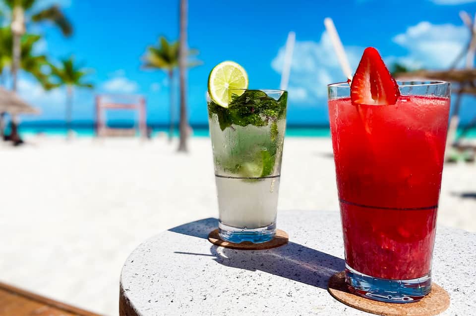 Two colorful cocktails with lime and strawberry garnishes on beach with ocean backdrop