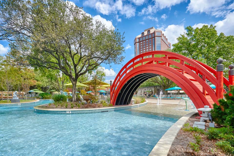 Resort pool with red arched bridge, waterfall fountain, palm trees, and mountain views