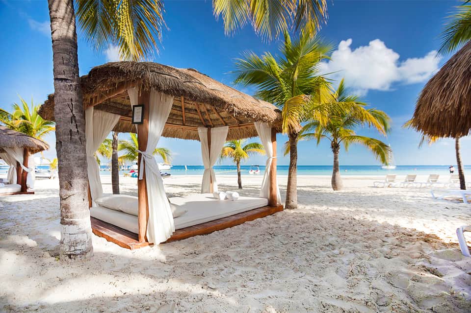 Luxurious beach cabana with thatched roof, white curtains, and palm trees on white sand