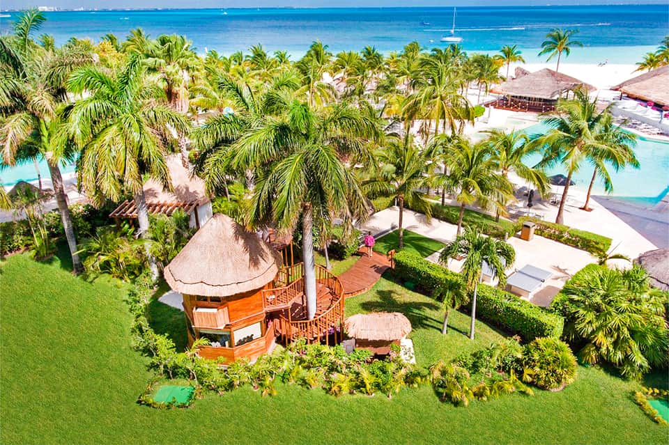 Aerial view of tropical resort with orange bungalow, palm trees, pools, and white sand beach