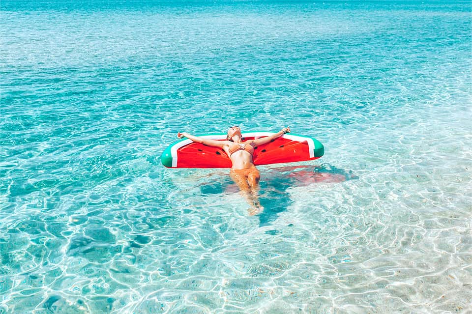 Woman floating on red inflatable in crystal-clear turquoise shallow water