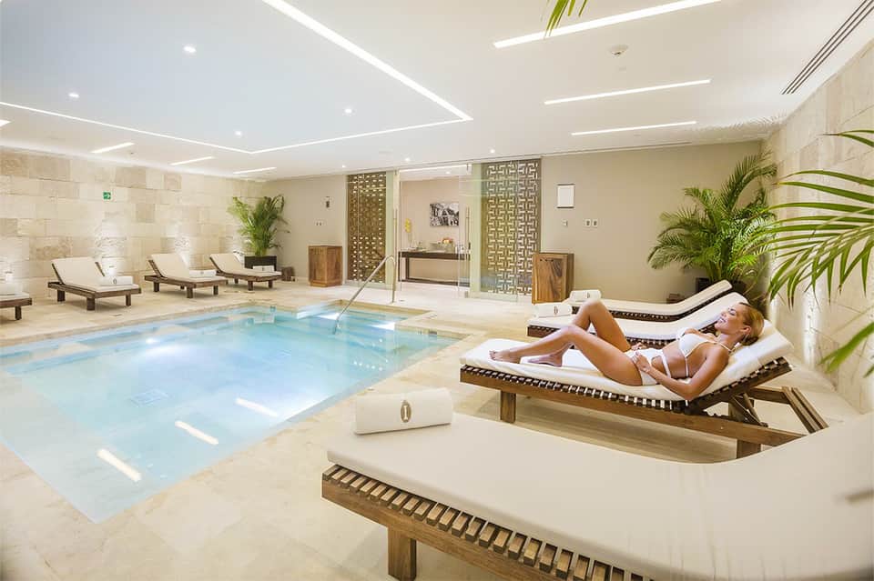 Indoor spa pool with modern ceiling, lounge chairs, and stone wall accents