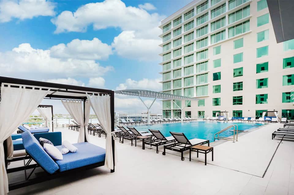 Resort pool area with cabanas, lounge chairs, and multi-story hotel building