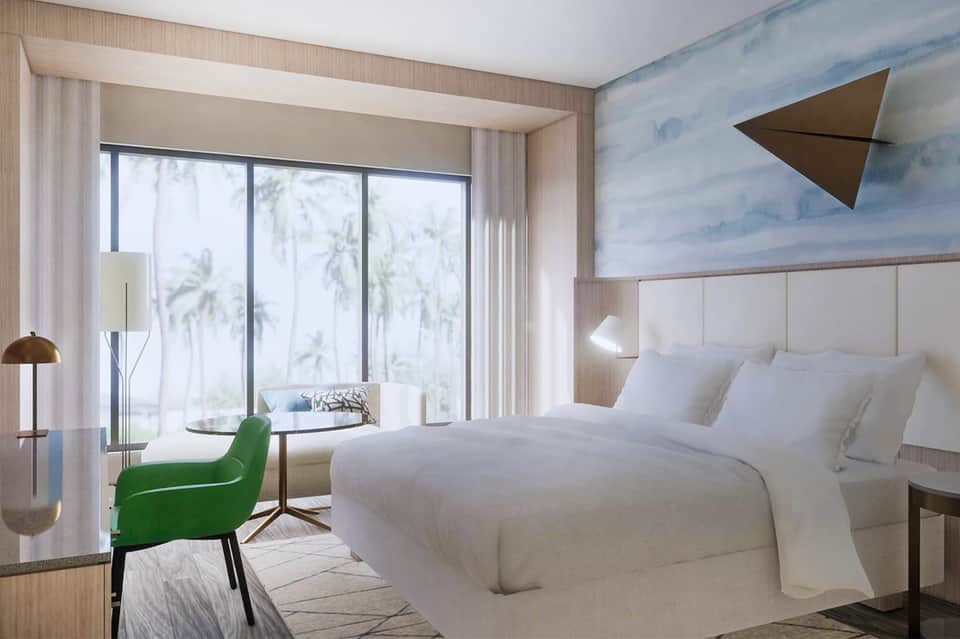 Modern hotel bedroom with white bedding, green accent chair, ocean view, and beach-inspired wall art