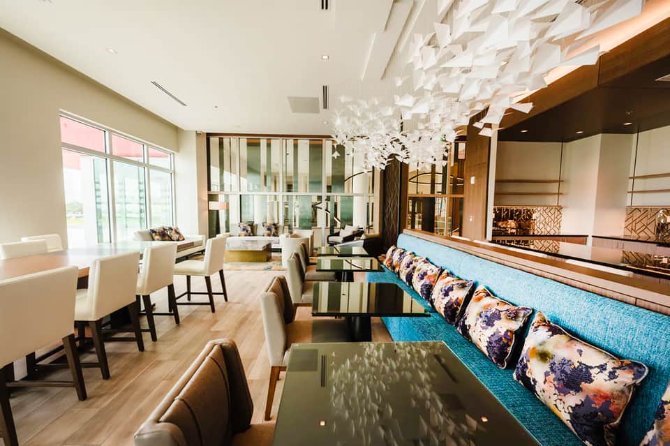 Modern hotel lounge with high ceilings, colorful pillows, wooden accents, and floor-to-ceiling windows