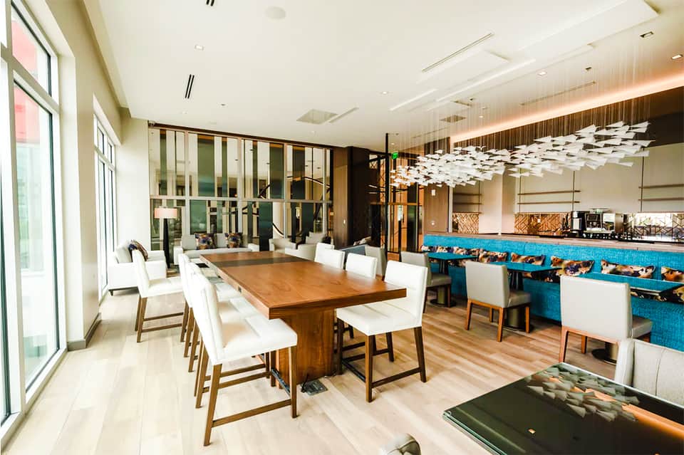 Modern hotel dining room with wooden table, white chairs, blue bar, and large windows