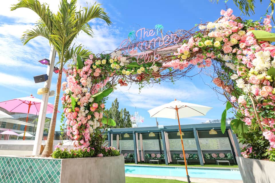 Floral archway entrance to The Meritage Club with pool and umbrellas in background