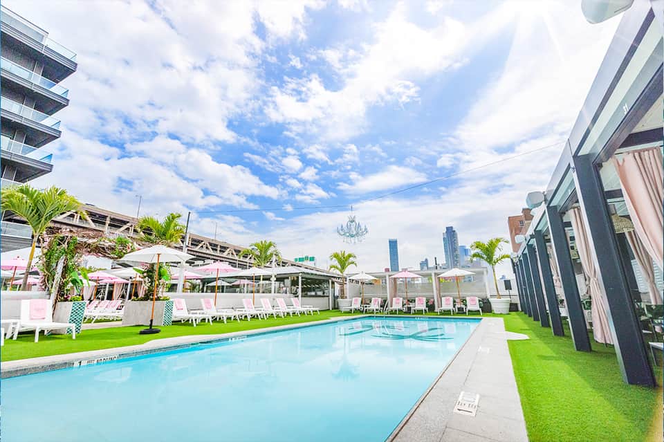 Rooftop pool with city skyline, lounge chairs, umbrellas, and manicured lawn