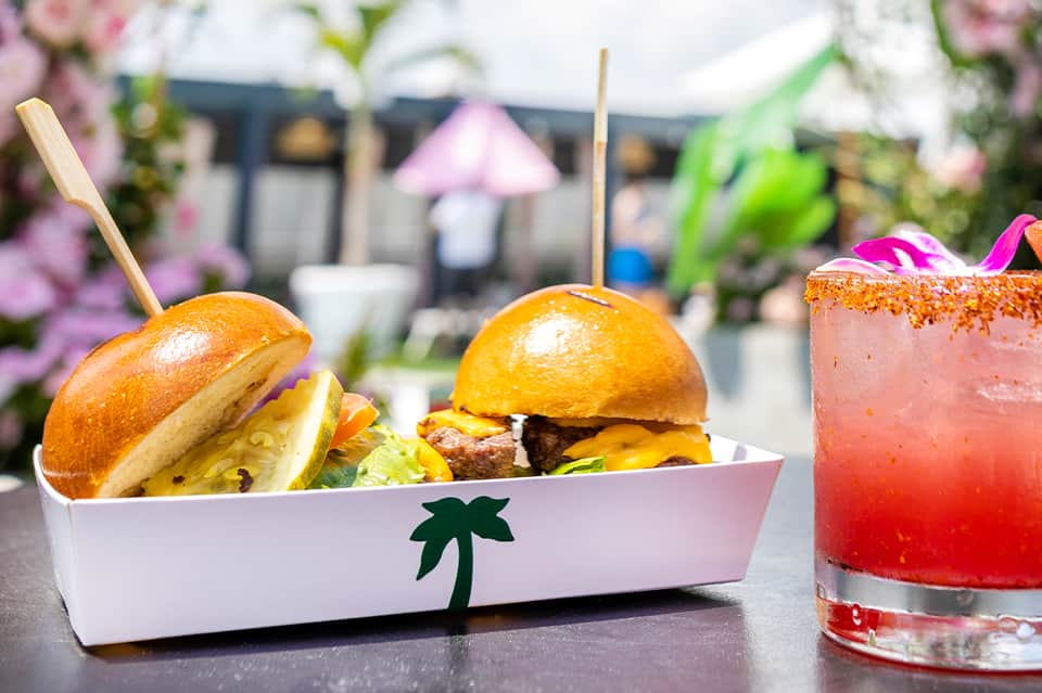 Gourmet burgers and tropical cocktails served poolside with pink flowers in background